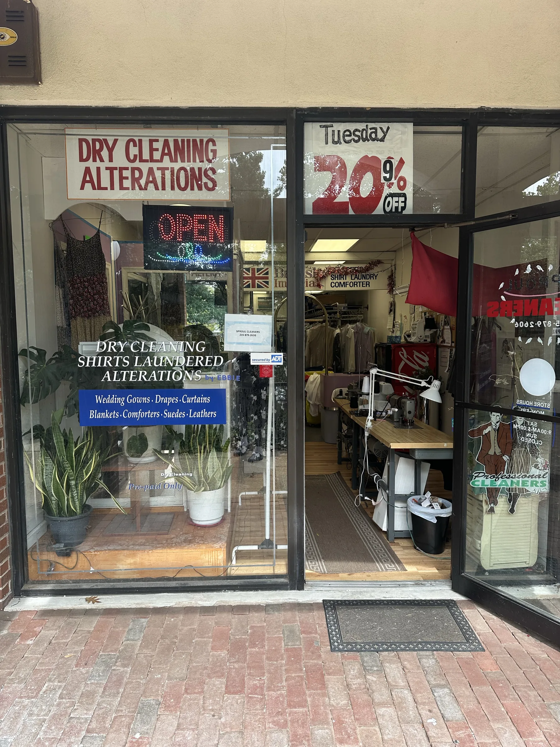 Open entrance to Sproul Cleaners with window signs advertising dry cleaning, shirt laundering, and alterations.
